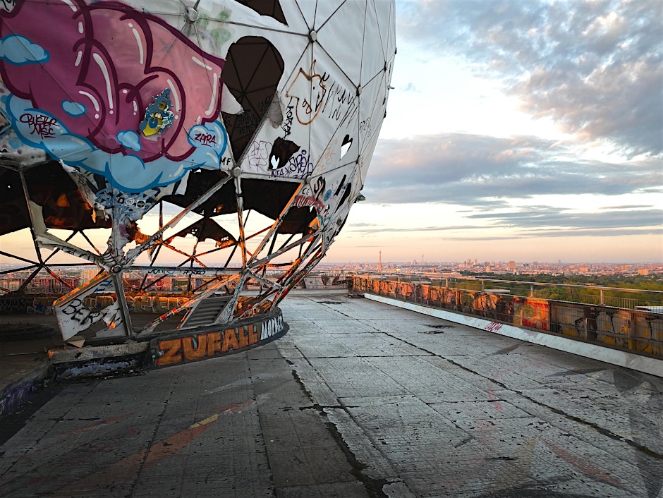 https___cdnevbuccom_images_1124185863_2155514222563_1_original - URBAN UTOPIA Graffiti-bedeckte Struktur auf einem Dach mit Blick auf eine Stadtlandschaft bei Sonnenuntergang.